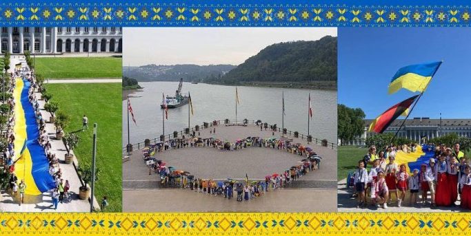 Menschen mit ukrainischen Flaggen bilden ein Herz am Wasser, umgeben von Feierlichkeiten.