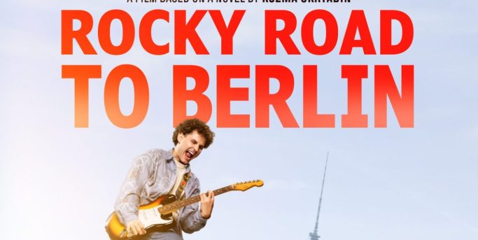 Ein Musiker spielt Gitarre vor einem Berliner Wahrzeichen mit dem Titel "Rocky Road to Berlin".
