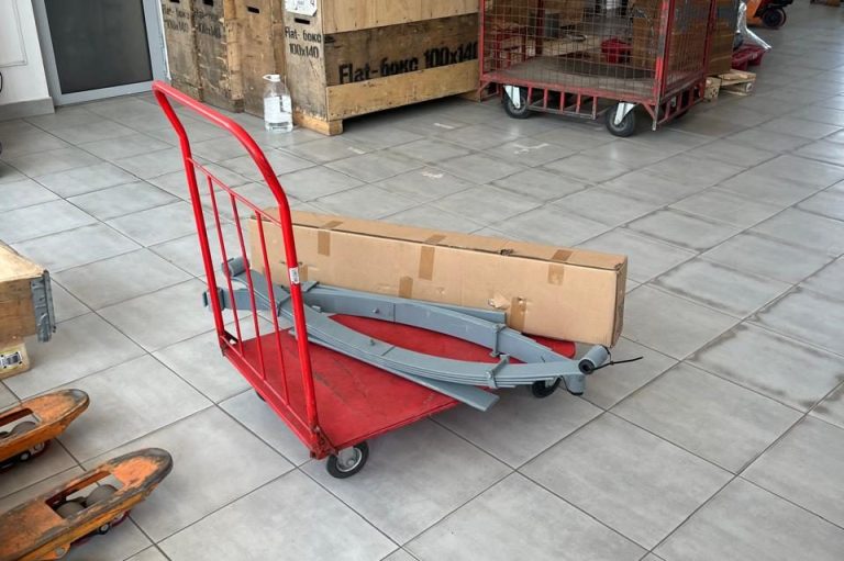 Rote Sackkarre mit grauem Gestell und Holzplatte auf einem gefliesten Boden.