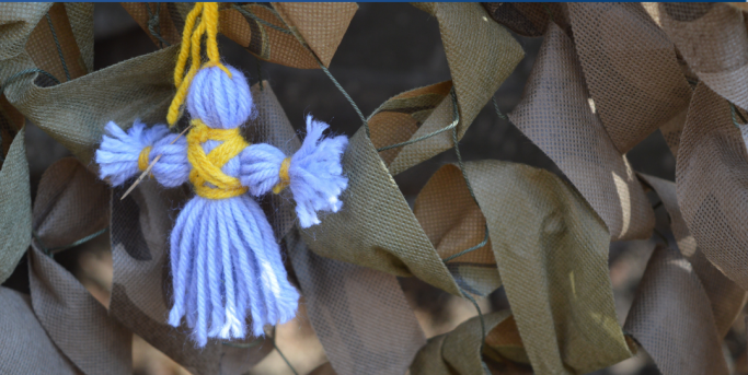 Blauer Stoffanhänger mit gelbem Band, umgeben von braunen Blättern.