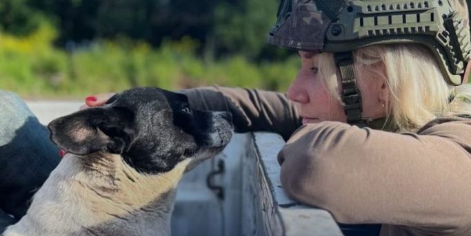 Frau mit Helm interagiert liebevoll mit einem Hund im Freien.