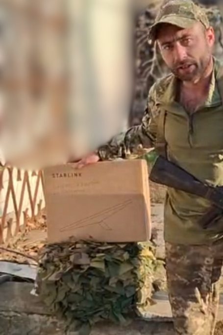 Soldat hält eine Holzbox vor einer bewachsenen Umgebung.